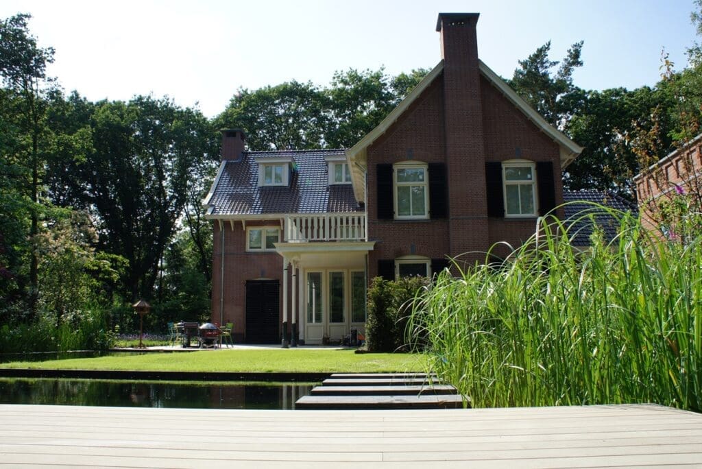 mooi aanzicht vanaf de vlonder naar het huis met daar tussen de zwemvijver het gazon en het terras