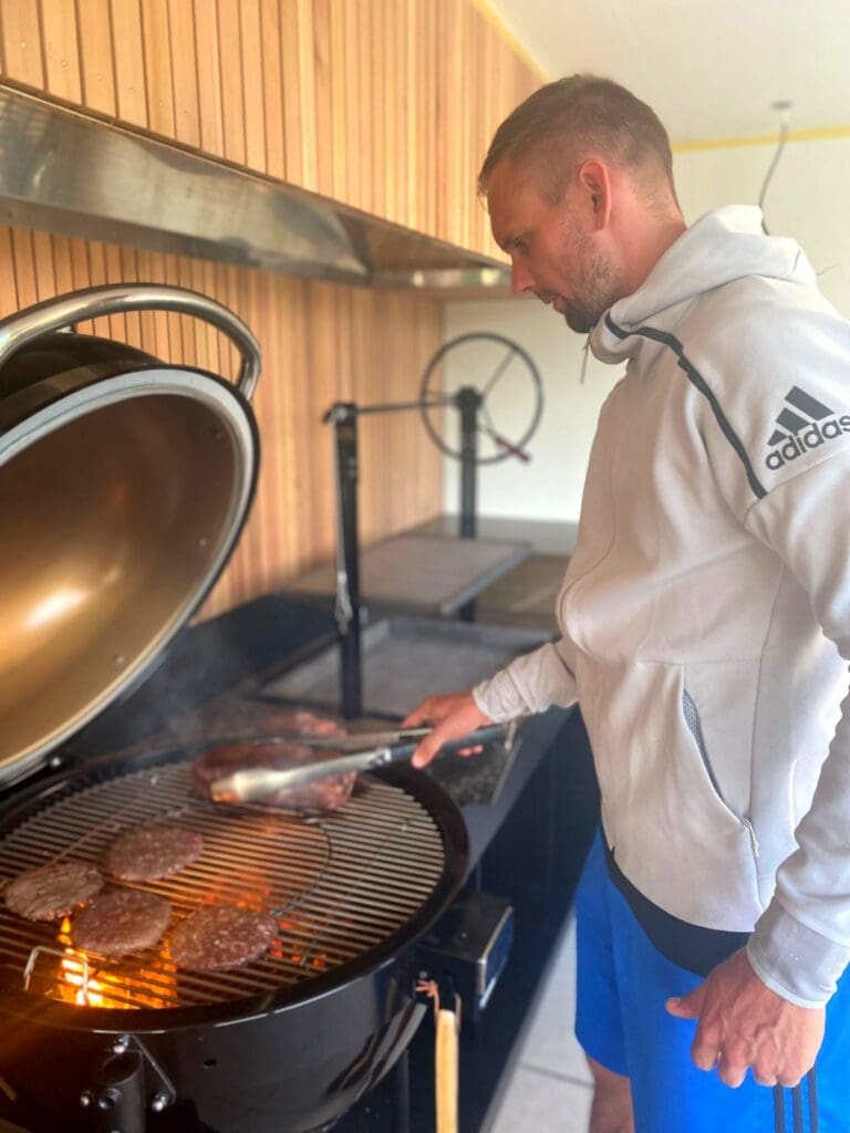 Man die het vlees omkeert op de bbq in luxe buitenkeuken