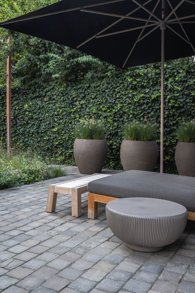 ligbed op het terras onder de parasol met er achter potten gevuld met grassen