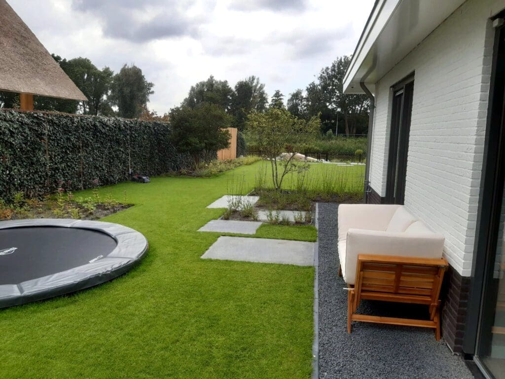 zijtuin met staptegels in het gazon en een trampoline