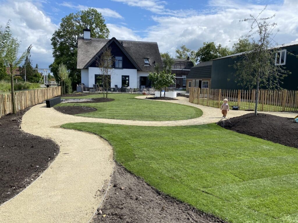 Landelijke tuin in aanleg met zandkleurig padvast, borders en gazon.