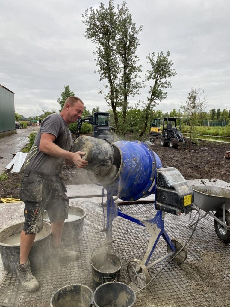 Lachende werknemer is beton aan het mixen voor Romfix bestrating.