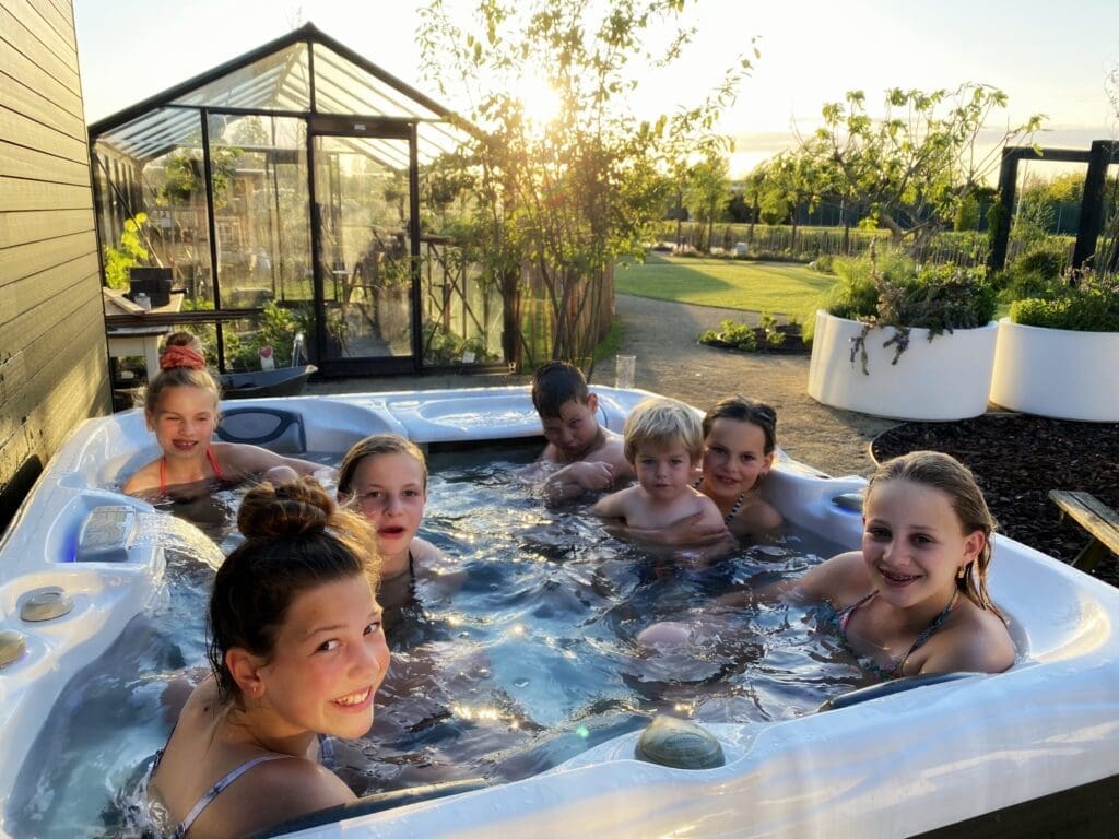 Groep kinderen in bubbelbad buiten in landelijke tuin.