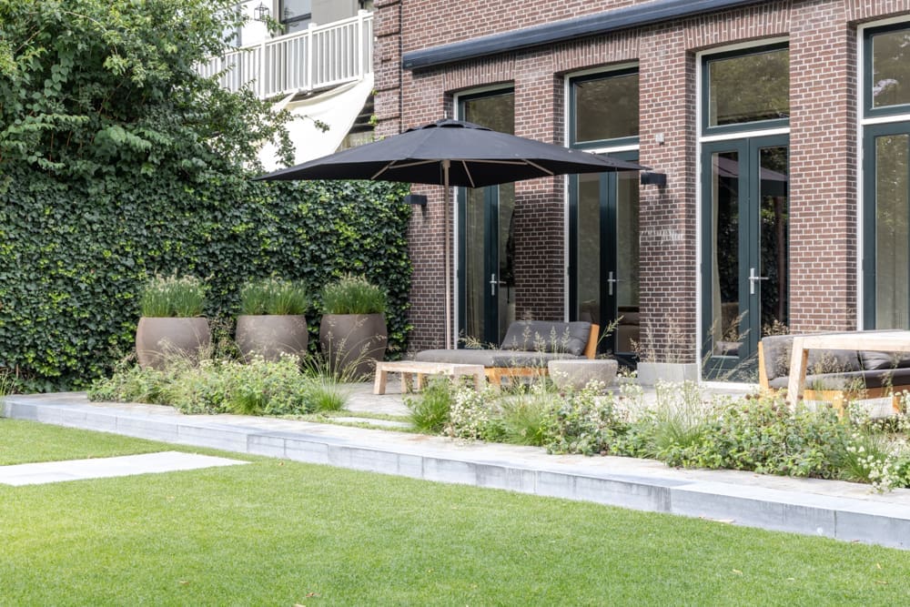 groot terras aan het huis met ligbed onder de parasol en eettafel