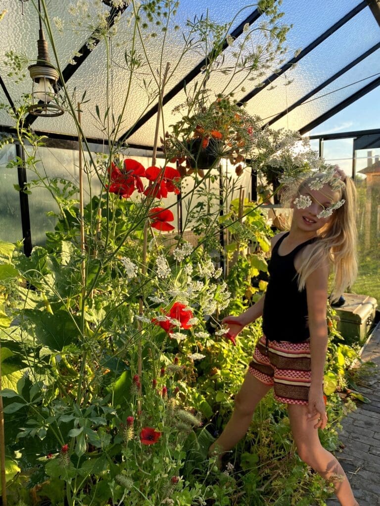 Tienermeisje in moestuinkasje te midden van grote groenteplanten en bloemen.