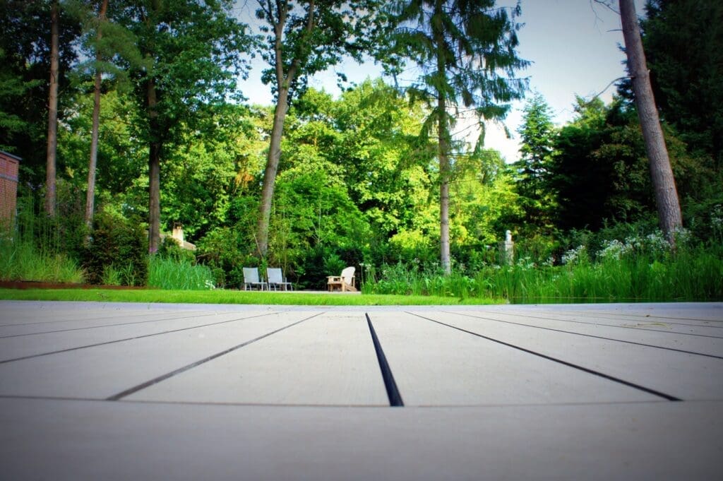 close-up van kunststof vlonderplan met mooie groene tuin met het gazon de groene borders en de bomen