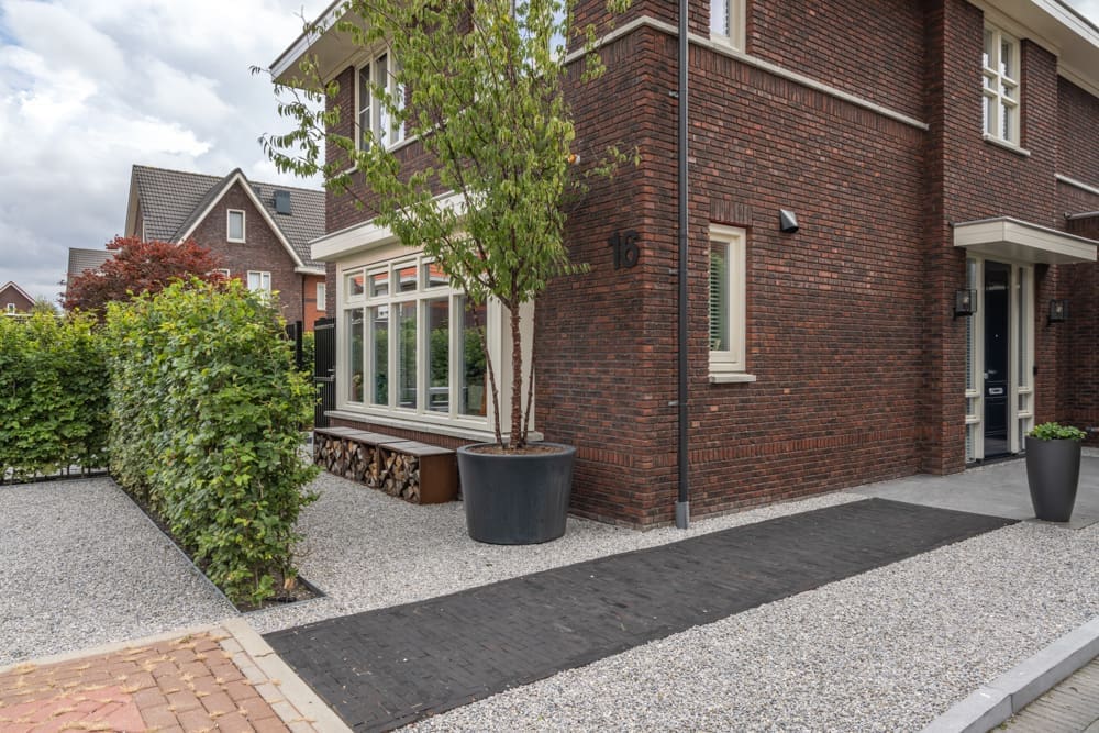 klinkerpad door het grind heen naar de voordeur langs de pot met een boom er in