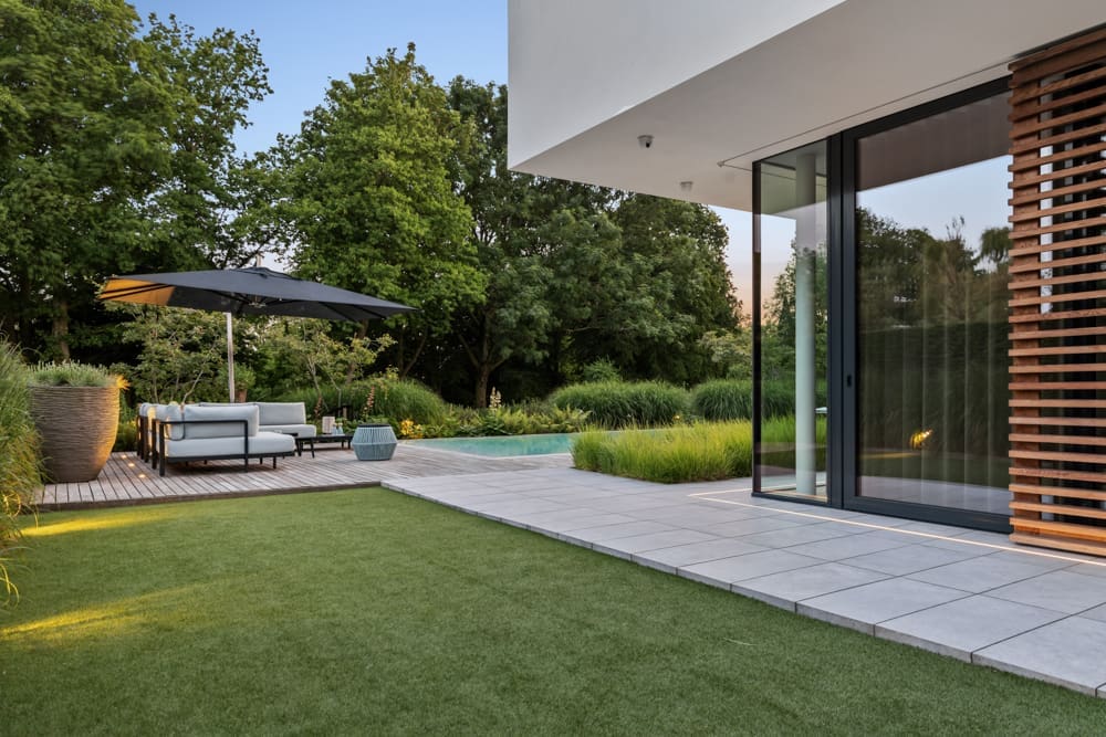 zijtuin met groot kunstgras vlak en tegels langs het huis naar de vlonder toe