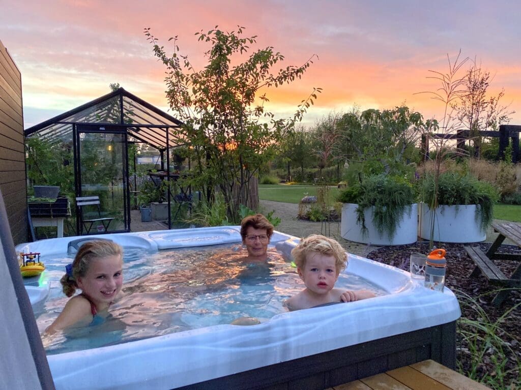 Familie in jacuzzi buiten met ondergaande zon in landelijke tuin.