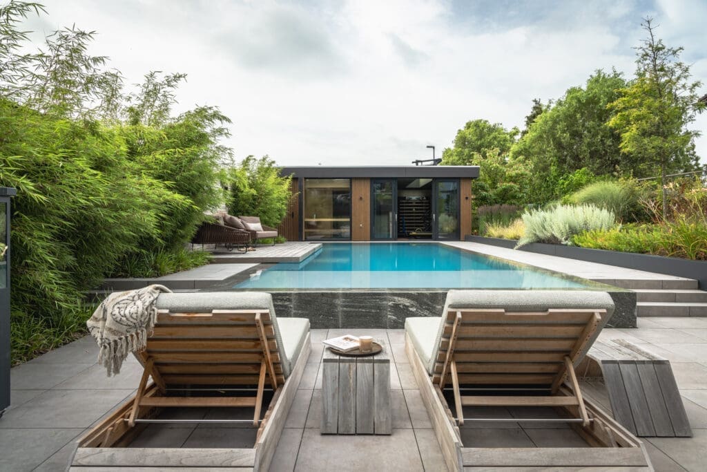 twee ligbedjes aan het zwembad met daar achter een poolhouse
