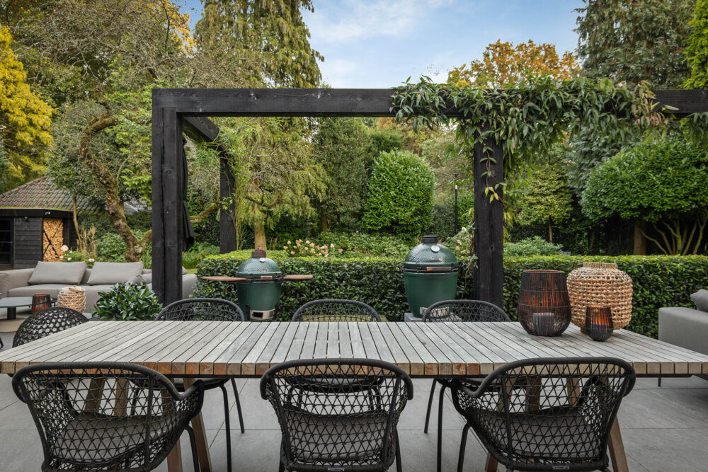 de eettafel met op de achtergrond de robuuste pergola en de Big Green Eggs.